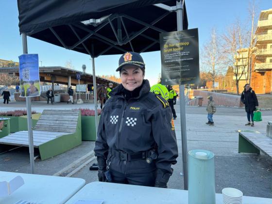 Politibetjent står foran en stand på Mortensrudtorget og smiler
