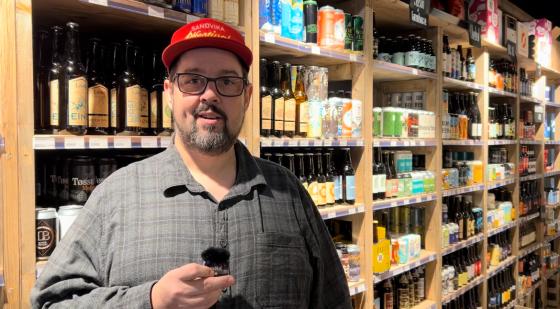 Mann foran en hylle med øl iført caps.