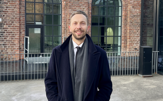Mann i frakk smiler foran Kunsthøgskolen i Oslo