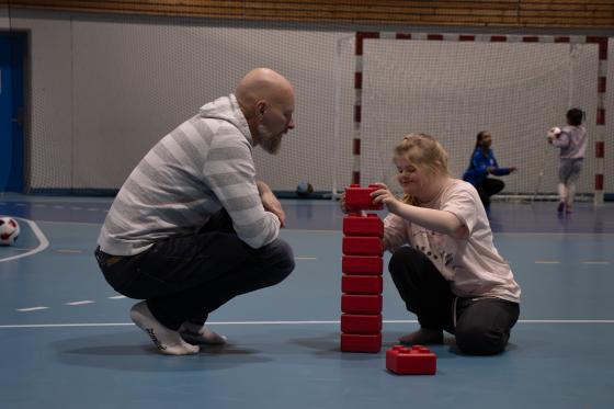 Far og datter som leker med store legoklosser sammen i en idretshall. 