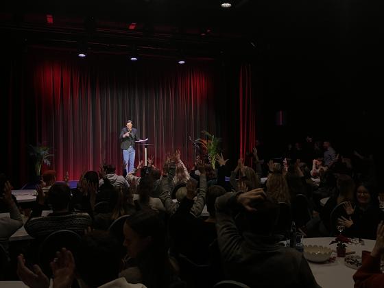 En mann står på scenen og snakker tegnspråk, men publikum et fullsatt applauderer