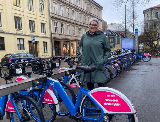 En dame står ved masse sykler og smiler.
