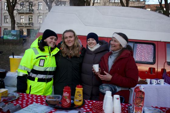 fire damer står og smiler bak kaffebordet. I bakgrunnen er en rød og hvit van 