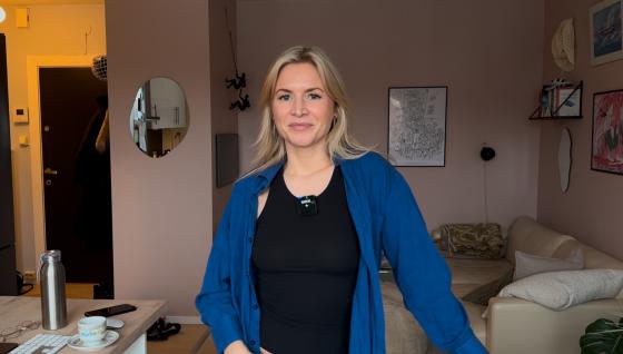 Kornelia Minsaas står i stuen sin ikledd en blå skjorte