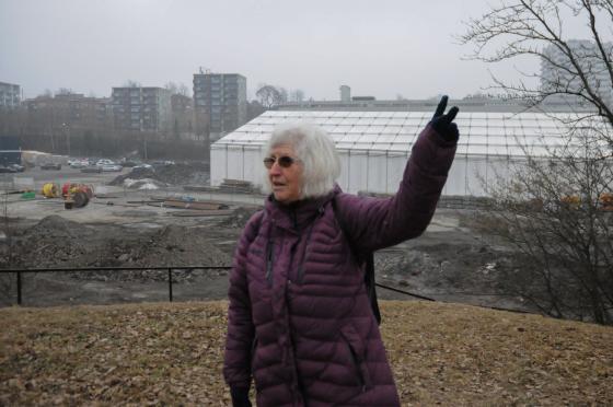 En dame med lilla boblejakke forteller om byggeplassen man ser bak henne