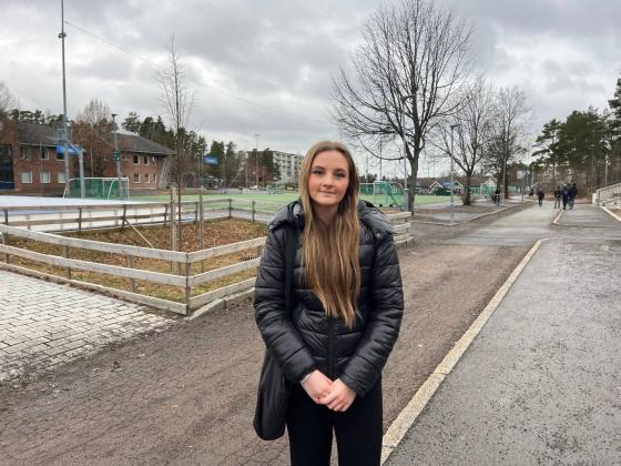 Jente som står i skolegård med hendene foldet