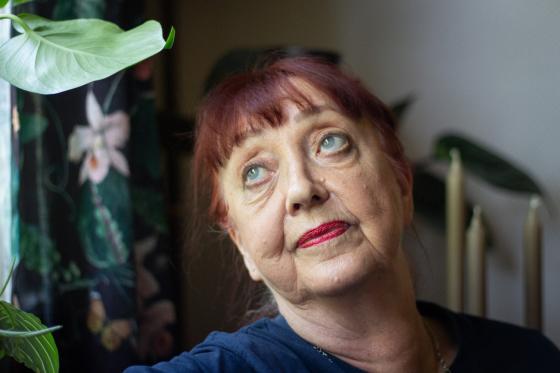 Portrett av en eldre dame med rødt oppsatt hår og pannelugg. Hun har blikket rettet mot et vindu. I bakgrunnen ser man en plante, noen lys og gardiner