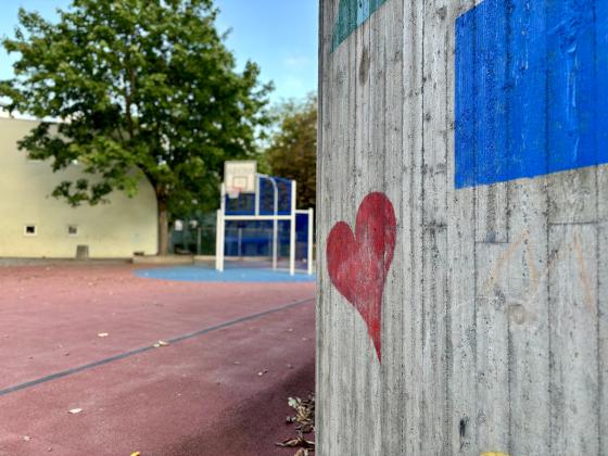 Et hjerte på en vegg, med en basketball bane i bakgrunnen i en skolegård