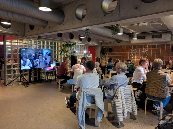 Studenter sitter rundt bord og ser på valgsendingen til NRK