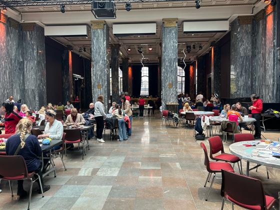 Deltakerne på Håndverksdagen på Sentralen er samlet rundt bord i Marmorsalen hvor de holder på med ulike typer håndverk. 