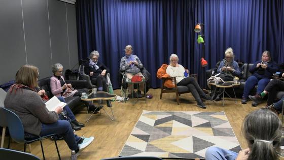 Personer sitter i ring og strikker.