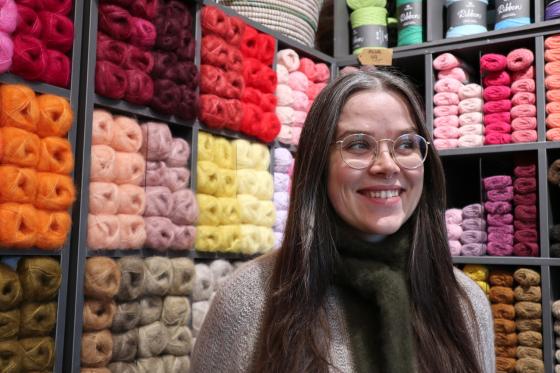 Dame som står foran en vegg av garn og smiler