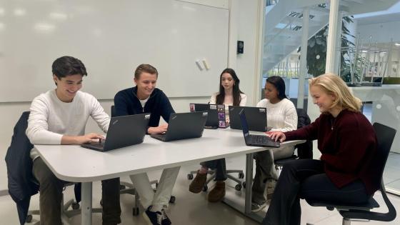 Fem elever sitter på et grupperom og arbeider.