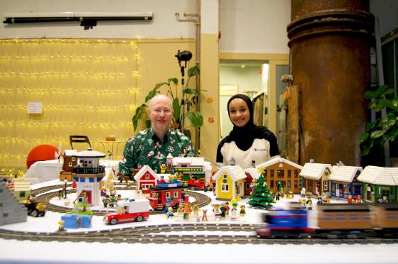 Jaleela og Roy sitter foran utstilling på lego-marked. 