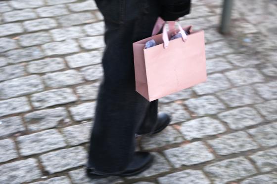 Person som går på fortauet med en rosa papirpose i hånden.