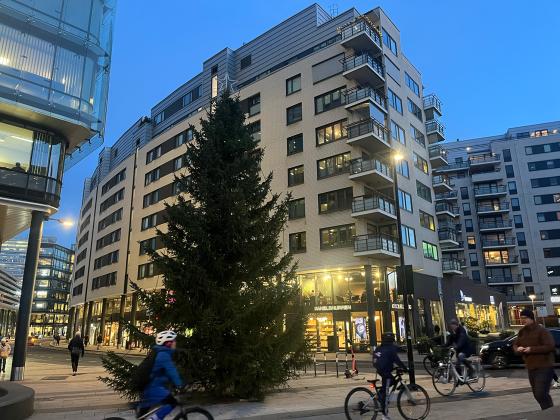 Et juletre foran starten av Karenlyst Allé rett utenfor togstasjonen på Skøyen. Folk går forbi. Det er litt mørkt. 