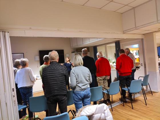 Nordstrand demenskor synger - De står oppreist med ryggen til kamera, koristen synes foran