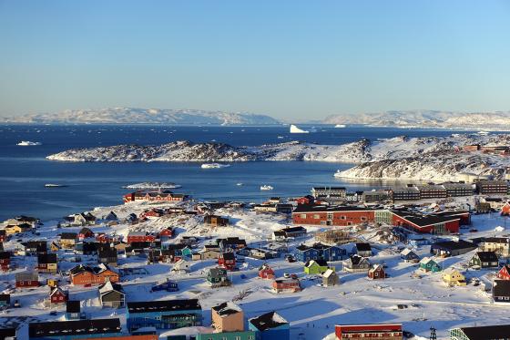 Fargerike hus st&aring;r i sn&oslash;dekket landskap. Det er mulig &aring; se hav og fjell