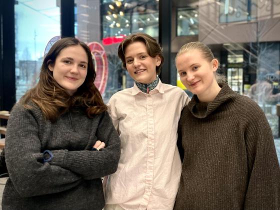 Tre unge kvinner st&aring;r sammen og smiler.