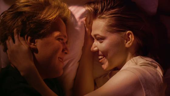 En gutt og jente ligger i en seng og ser p&aring; hverandre.