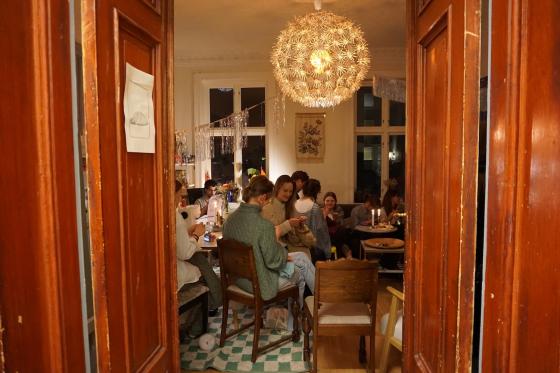 Gjennom d&oslash;ren ser man mennesker som fyller rommet mens de strikker og syr