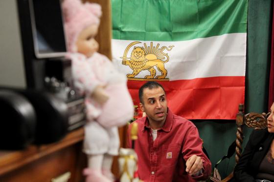 En mann sitter &aring; diskuterer foran et Iransk flagg