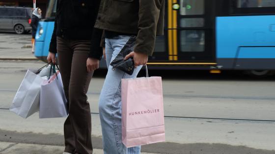 handleposer blir holdt av to jenter bildet er tatt fra livet og ned. ser trikken i bakgrunn