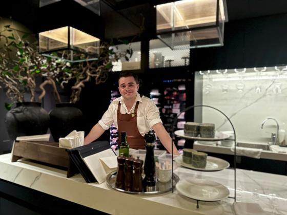 Mann med forkle i vinbar som lener seg p&aring; disken