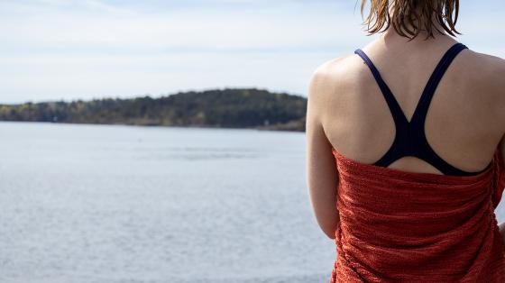 Et bilde av en dame i badedrakt og h&aring;ndkle tatt bakfra i forgrunnen Viser Oslofjorden i bakgrunnen.