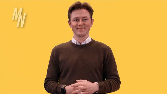 Mann i brun genser st&aring;r foran en gul green screen bakgrunn.