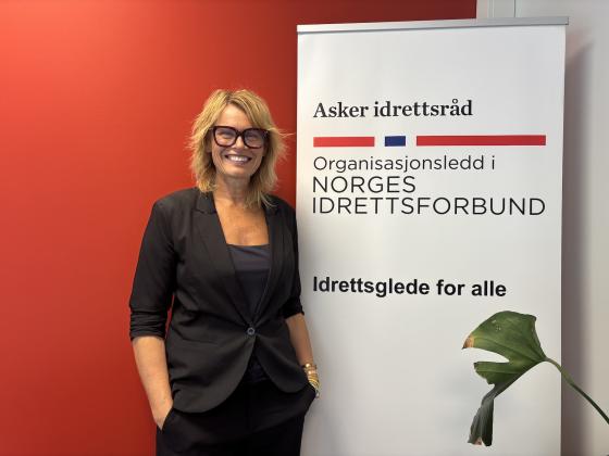 Gry Elisabeth Garlie, daglig leder i Asker idrettsr&aring;d, ved siden av en plakat