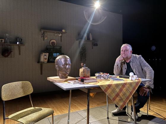 En mann og en byste av en annen mann på sitter på et bord. 