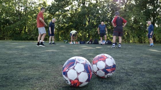 To fotballer i forgrunnen hvor de i bakgrunnen gjør seg klar for trening
