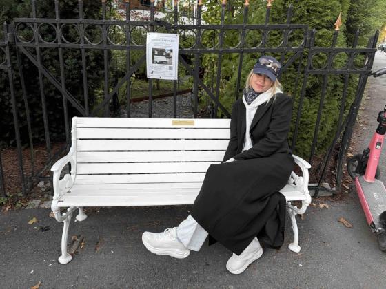 En jente iført en svart kåpe sitter på frognerbenken