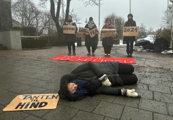 Demonstrant ligger på bakken med et skilt som sier "Tanten til Hind". I bakgrunnen ser man flere demonstranter som holder skilt med budskapet om at Israel må boikottes fra Eurovision.