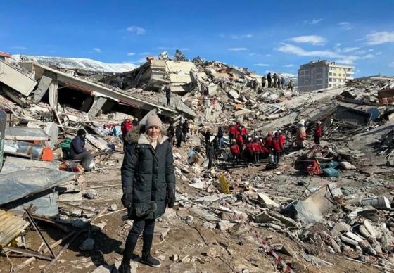 Journalist Åse Marit står i ruinene etter jordskjelvet. Bek henne foregår redningsarbeid. 