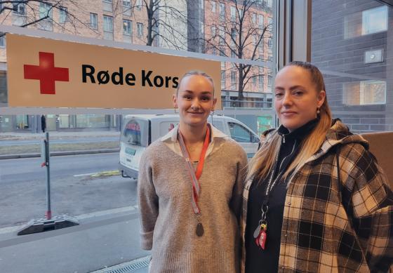 Seniorkonsulenter i Barnas Røde Kors, Martine Jakobsen og Marielle Halvorsen, avbildet i Røde Kors' lokaler i Hausmannsgate 23, foran et Røde Kors-skilt.