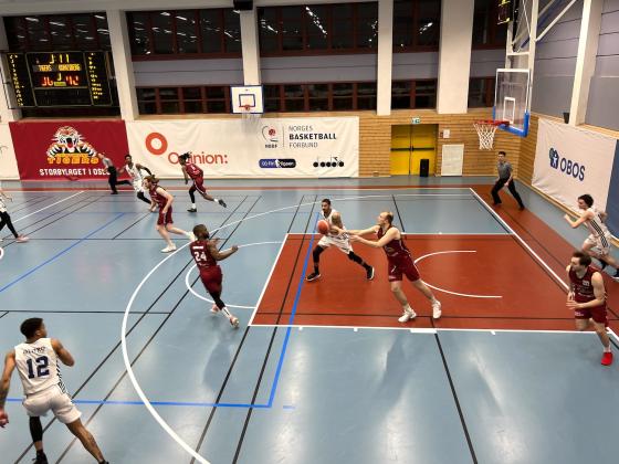 Spillere på en basketball bane som springer mot ballen. 