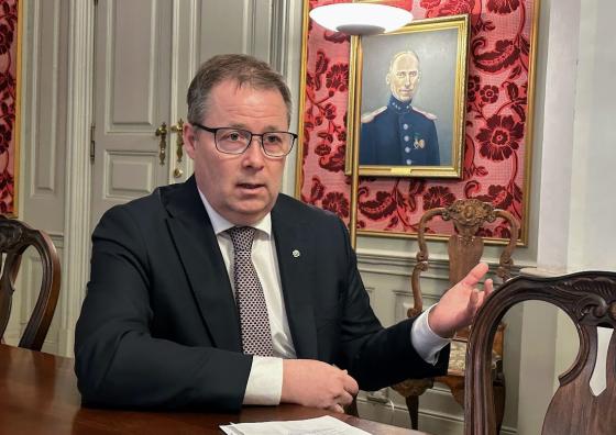 Forsvarsminister Bjørn Aril Gram sitter ved et gammelt trebord med gamle malerier hengende i bakgrunnen. 