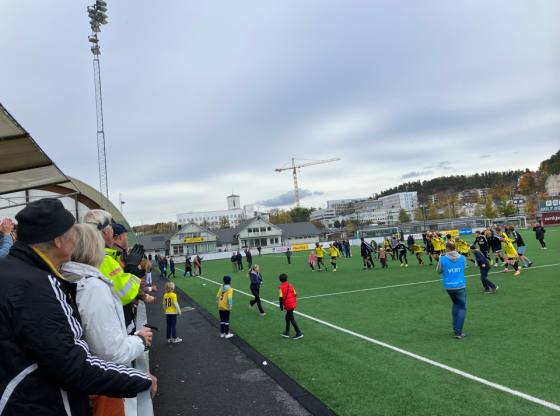 Bilde fra Sandvika Stadion. Bærum sine alagsspillere er stilt opp på rekke, holder hverandre i hendene, og er på vei til å gjøre den såkalte bølgen overfor gjenværende fans på tribunen etter kampen mot Træff.