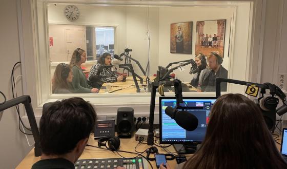 Mennesker sitter overfor hverandre og snakker i et radiostudio. 