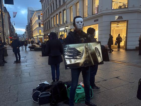 En mann med maske holder en tv-skjerm som viser videoer av dyr som blir mishandlet og slaktet på norske gårder 