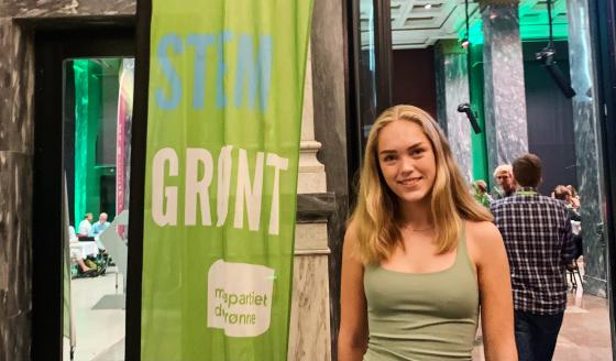 Portrettbilde av Helena Bugge, representant for Grønn ungdom, foran et banner av MDG sin logo, ved valgvaken i Oslo