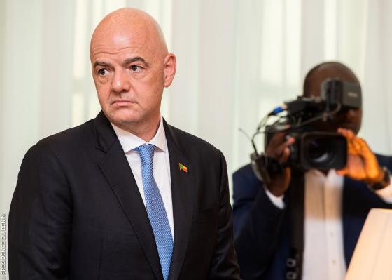 Bilde av Gianni Infantino i en svart dress med blått slips og en kameramann i bakgrunn.