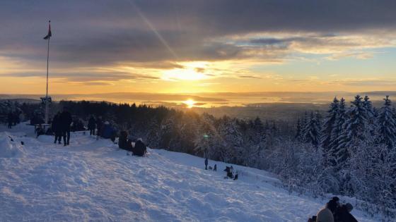 solnedgang på toppen av Grefsenkollen i Oslo. Mennesker og snø, flagstang