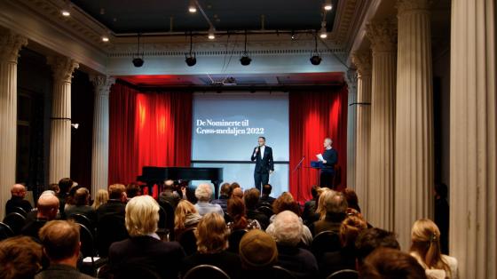 Mann står på scene for å presentere vinnere av grøssmedaljen