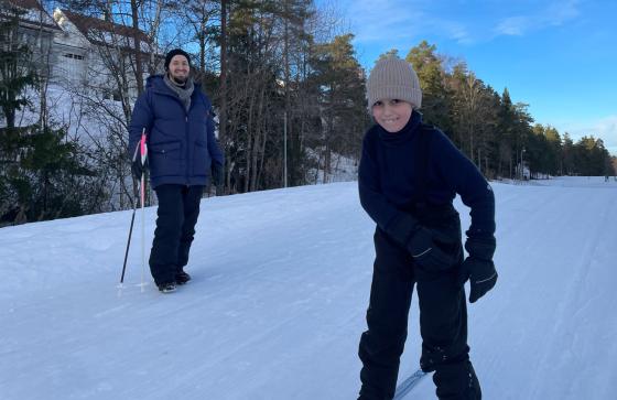 Gutt som står på ski med faren i bakgrunn.