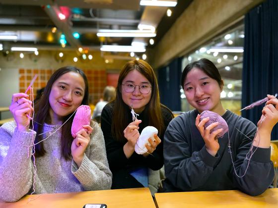 Haruno Eda, Wakana Kawamura og Kak Fung Cheunh smiler til kameraet og viser frem det de har strikket. 