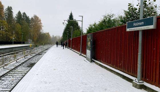 Det snør på Holmen T-banestasjon. Reisende venter på T-banen.