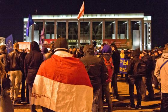 Et kveldsbilde, hvor hviterussiske demonstranter er samlet på et torg og bærer det hvite og røde flagget deres.